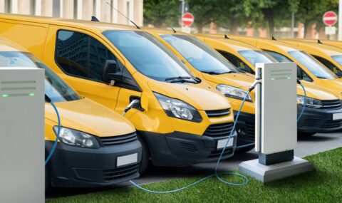 Row,Of,Yellow,Electric,Delivery,Vans,At,Charging,Stations,For