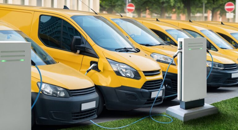Row,Of,Yellow,Electric,Delivery,Vans,At,Charging,Stations,For